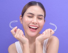 Woman smiling while holding two Invisalign trays
