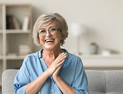 Senior woman with glasses smiling on couch at home