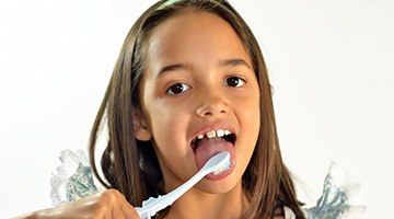 A young child brushing her tongue.