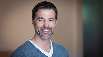 man in a gray sweater smiling with dental implants in Newark 