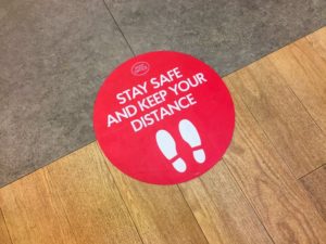 red sign on floor that reads "stay safe and keep your distance"