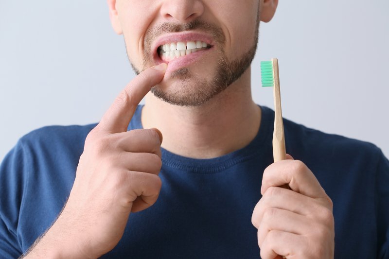 man holding toothbrush unhappily pointing at teeth