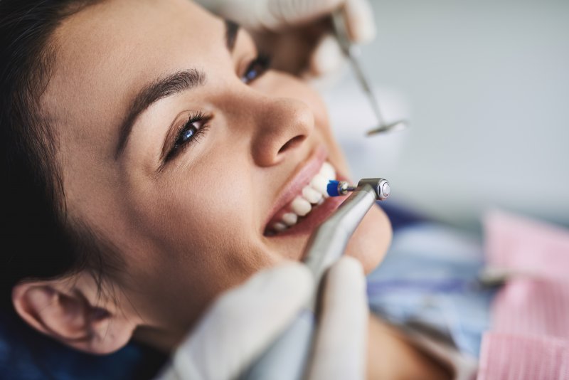 Woman smiling with teeth as dentist puts dental tools up to her grin