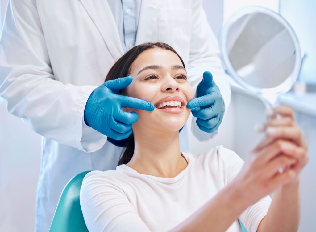 Dentist in blue gloves pointing to patient's smile as she looks in mirror